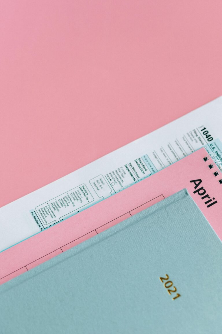 A close-up of tax forms with an April calendar on a pink surface, representing tax season.